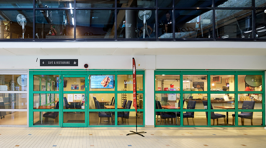 Ingång till Zeco Café från 50-metershallen på Valhallabadet. Inne på caféet finns bord och stolar.