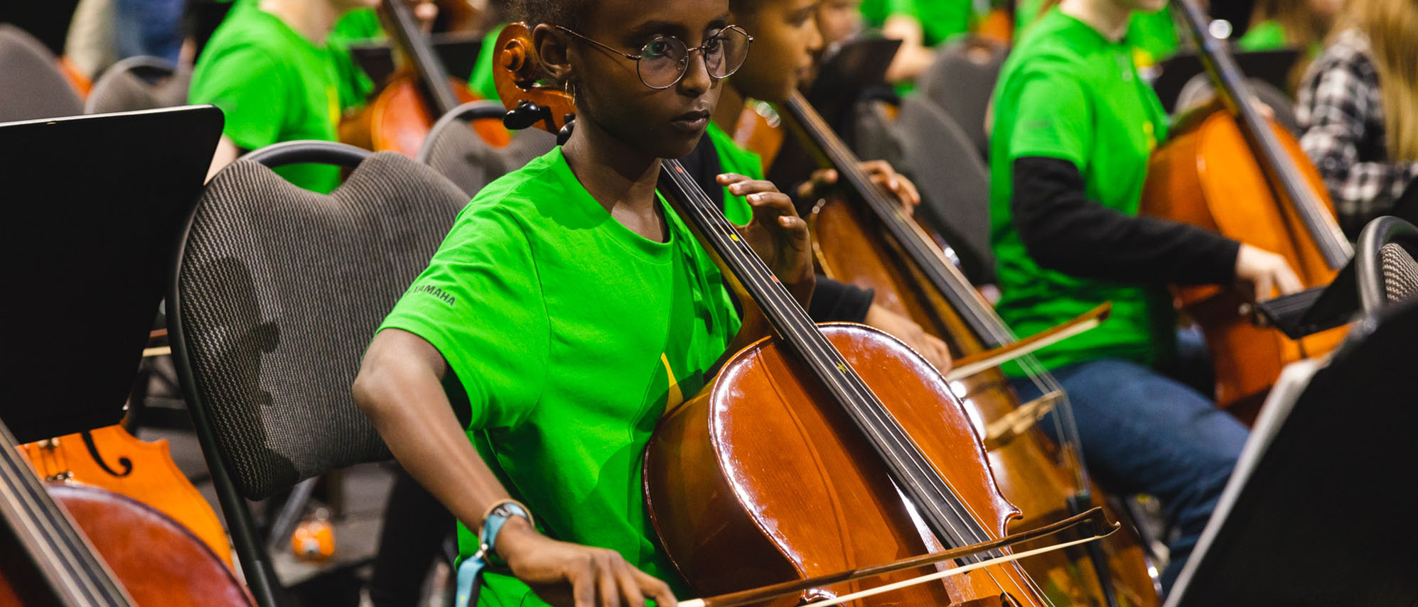 Ett barn sitter i en stor orkester och spelar cello.