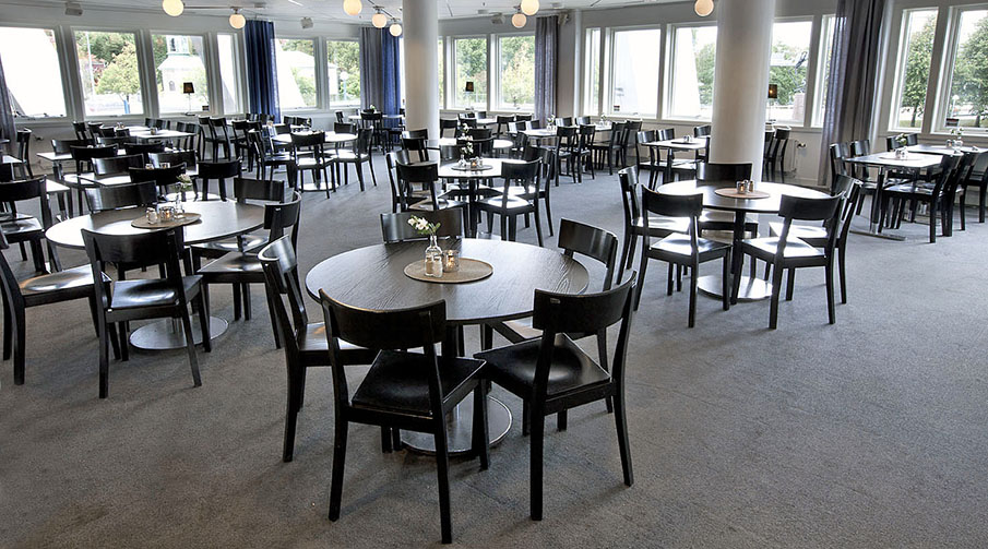 En ljus lokal med flera stolar runt runda bord i svart färg.