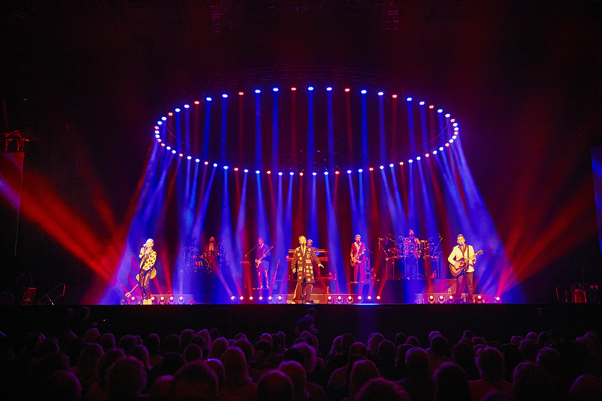GES står på scenen och sjunger. Ovanför är det ljus formade i en cirkel som lyser ner på dem.