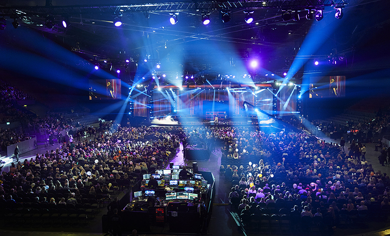 I mitten är scenen, publiken sitter runt omkring och det lyser lampor från scenen.
