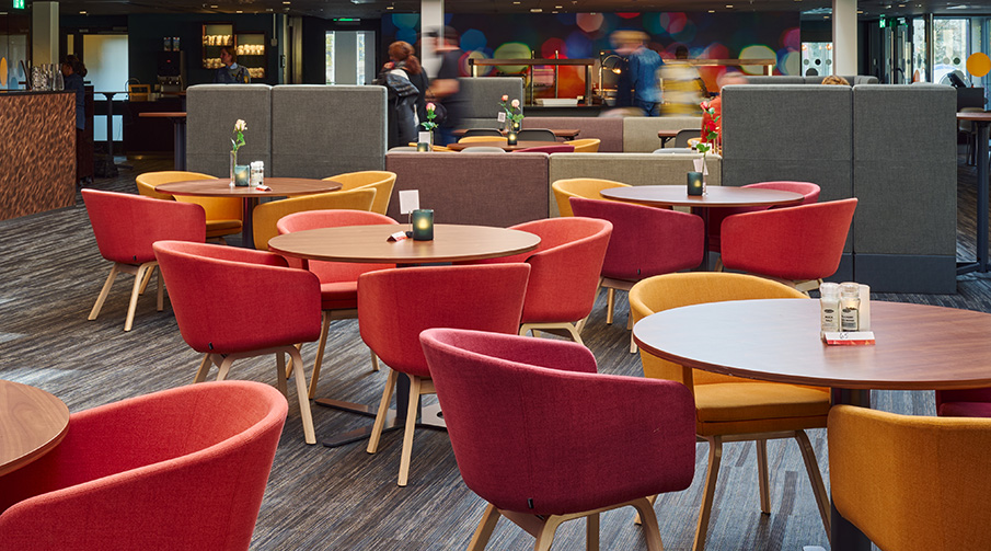 Restaurang med runda bord med röda och orangea stolar runt om.