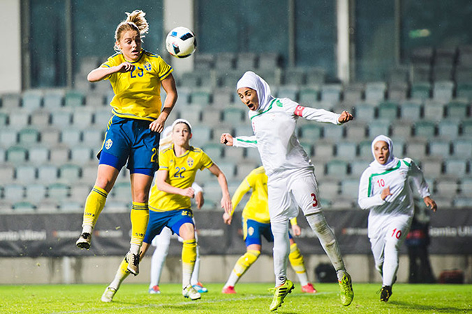 Irans spelare har nickat bollen mot en svensk spelare som hoppar högt upp i luften.