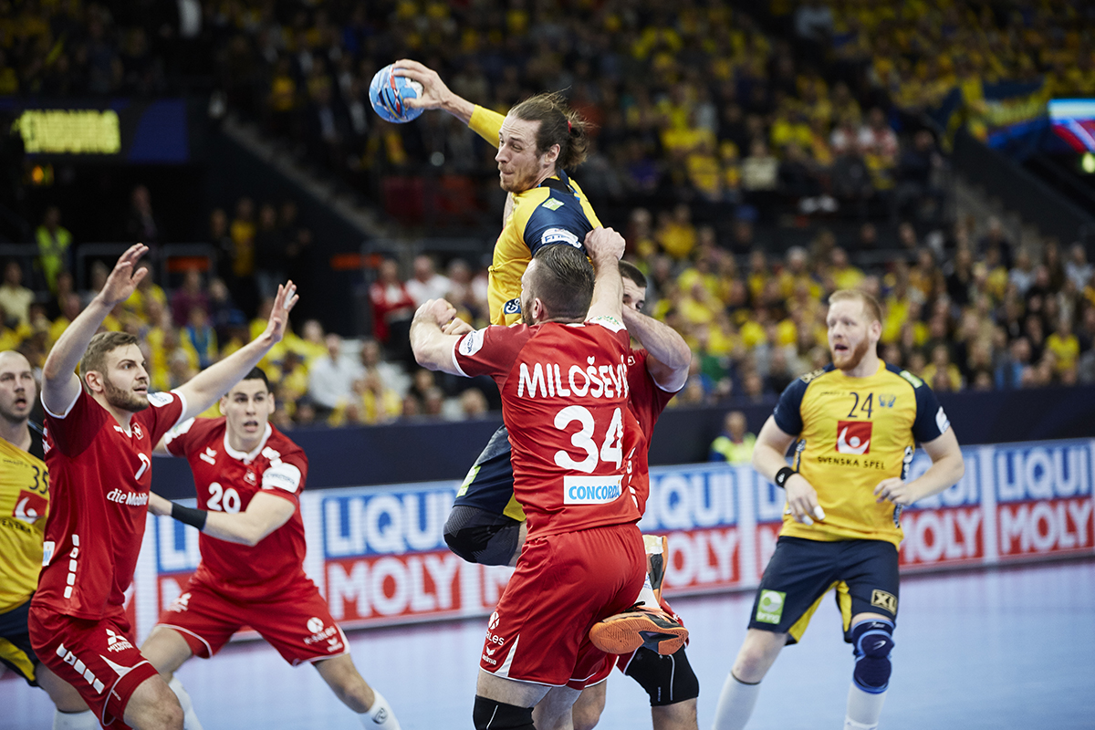 En svensk spelare skjuter på mål och en utländsk spelare försöker stoppa den svenska spelaren.